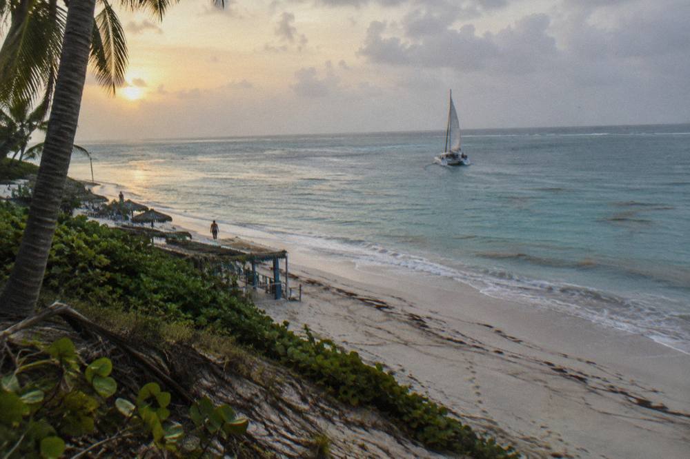 Wide view of a calm turquoise bay with a sailing catamaran heading toward open water