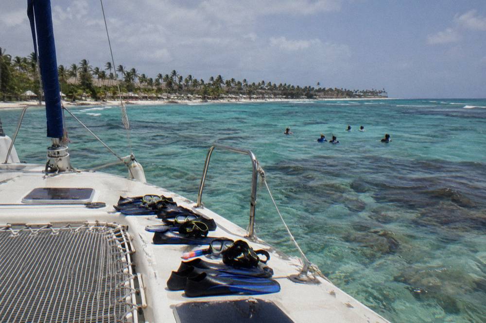Group of snorkelers in the water beside a moored catamaran in clear shallow water